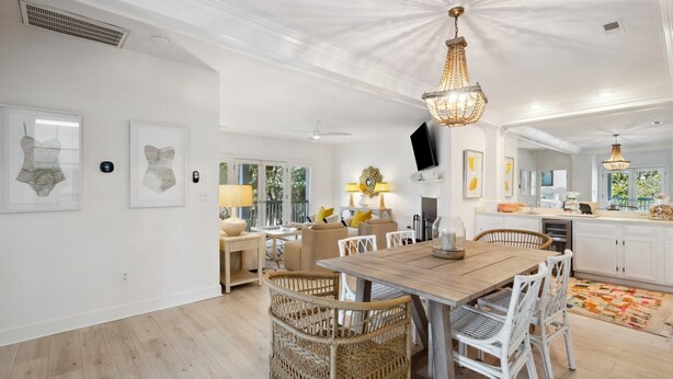 Un salón amplio con una mesa de comedor de madera rodeada de sillas de mimbre, un candelabro y obras de arte en las paredes.