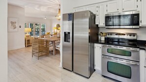 Una cocina moderna con electrodomésticos de acero inoxidable, armarios blancos y una zona de comedor con mobiliario de mimbre.