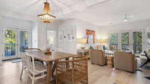Amplia sala de estar con una mesa de comedor de madera, sillas de mimbre, un sofá color beige y un ventilador de techo.