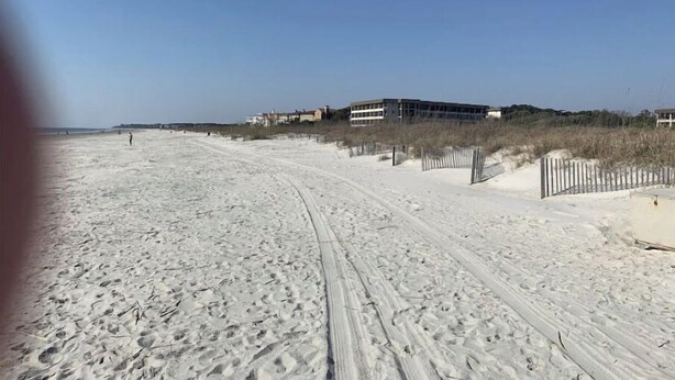 Een zandstrand met voetafdrukken en een hek.