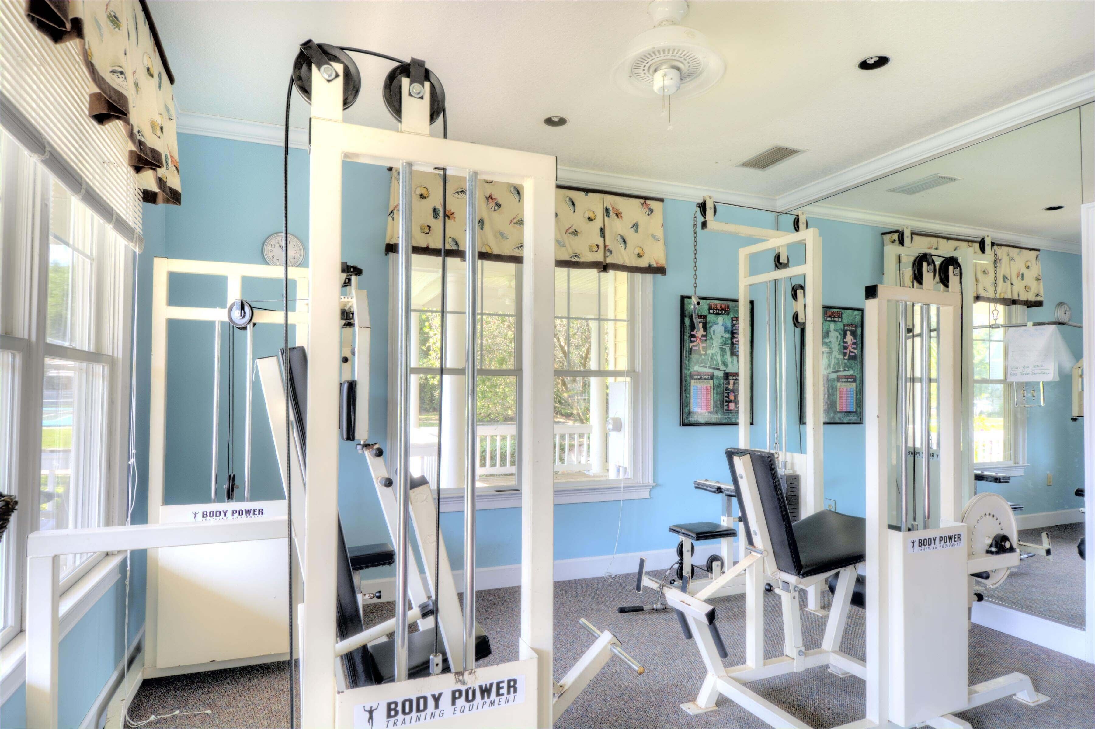 Un gimnasio con equipo de ejercicio, ventanas amplias y un espejo.
