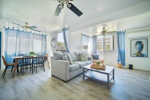 A living room with a sofa, dining table, chairs, ceiling fans, and a painting on the wall.