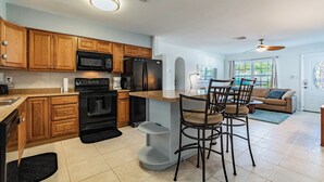 A modern kitchen with wooden cabinets, a black refrigerator, and a dining area with bar stools.