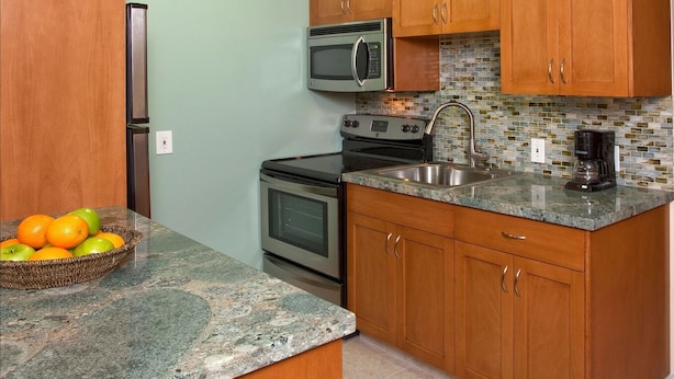 Una cocina con armarios de madera, microondas, estufa, fregadero y cafetera.