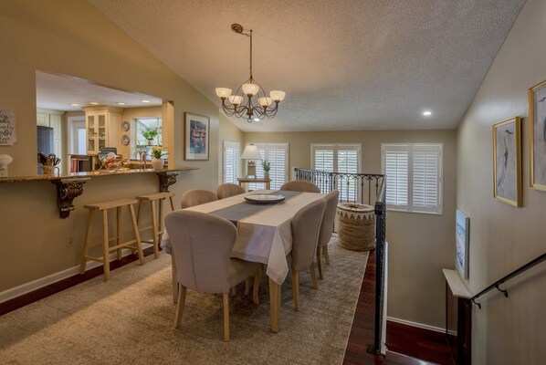 A dining area with a table set for four, a chandelier, and a kitchen in the background.
