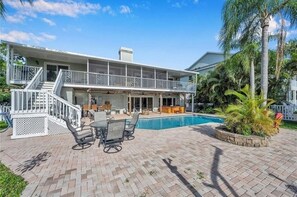 Una casa a due piani con patio coperto, mobili da esterno e piscina.