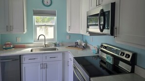 A kitchen with white cabinets, a stainless steel sink, a microwave, and a stove.