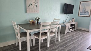 A dining area with a wooden table and white chairs, a basket with items, and a small cabinet with decorative items.