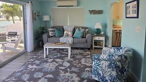 A living room with a ceiling fan, a grey sofa with patterned cushions, a patterned rug, a white coffee table, and a blue patterned chair.