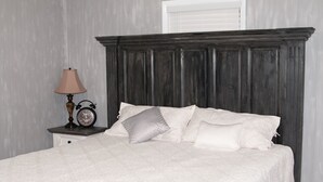A bedroom with a dark wooden headboard, a white bedspread, and a bedside table with a lamp and an alarm clock. - Cedar Mountain Lodge (Bryant)