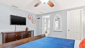 Een slaapkamer met een bed, een dressoir, een televisie en een plafondventilator.