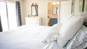 Une chambre à coucher avec un grand lit, une commode, un miroir et une salle de bain visible à travers une porte ouverte.