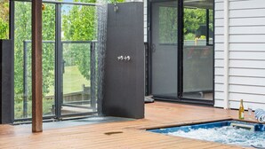 A hot tub with a waterfall feature, surrounded by wooden decking and a glass door leading to a garden. - KAMALA - MOUNT ELIZA (Mount Eliza)