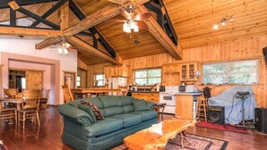 A spacious wooden cabin interior with a large green sofa, a wooden coffee table, and a kitchen area.