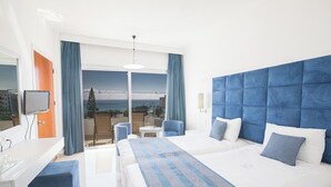 Habitación de hotel con una cama grande, un escritorio, una silla y un balcón con vista al mar.