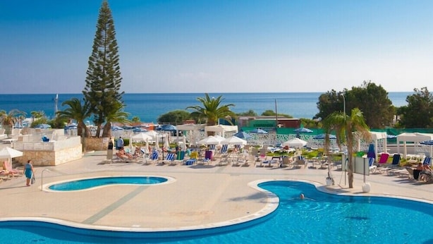 Zona de piscina con múltiples tumbonas y sombrillas, rodeada de palmeras y vistas al mar.
