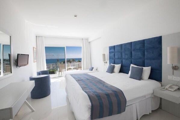 A modern hotel room with a large bed, a desk, a chair, and a view of the sea.