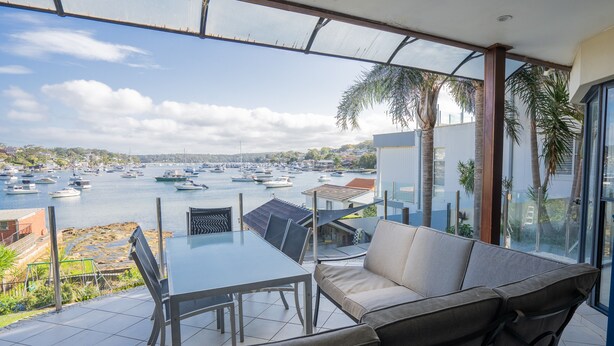 Una terraza con una mesa y sillas de vidrio, con vista a un puerto deportivo lleno de barcos.