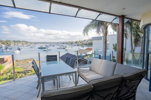 A terrace with a glass table and chairs, overlooking a marina with boats.