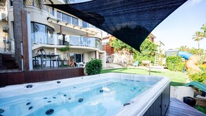 Un jacuzzi en una terraza de madera con vistas a un edificio residencial y un jardín con césped.