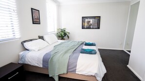 Un dormitorio con una cama, una mesita de noche, una planta en maceta y dos cuadros en la pared.