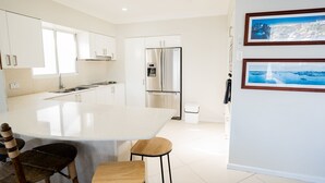 Una cocina moderna con armarios blancos, un refrigerador de acero inoxidable y una isla grande con taburetes.