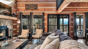 A cozy log cabin interior with a fireplace, comfortable seating, and large windows offering scenic views. - Mountain Views|Hot Tub|Foosball|Minicade (Pigeon Forge)