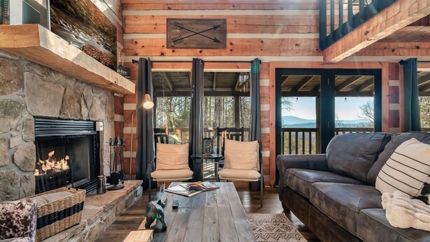 A cozy living room with a stone fireplace, leather sofa, and a wooden coffee table. - Mountain Views|Hot Tub|Foosball|Minicade (Pigeon Forge)