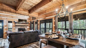 A wooden interior with a dining table set for a meal, a fireplace, and large windows overlooking a forest. - Mountain Views|Hot Tub|Foosball|Minicade (Pigeon Forge)