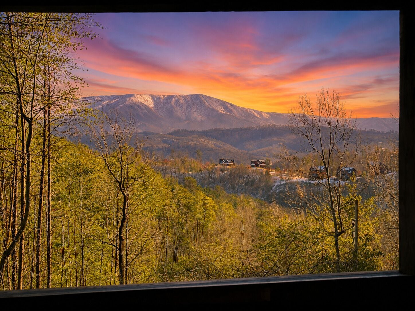 A mountainous landscape with a sunset, trees, and buildings in the valley.