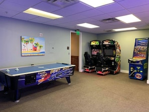 Una habitación con mesa de billar, dos máquinas de videojuegos y un cuadro en la pared.