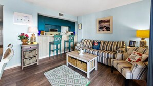 A living room with a striped sofa, a coffee table, and a kitchen in the background. - OCEAN VIEW- PETS ALLOWED! (Myrtle Beach)