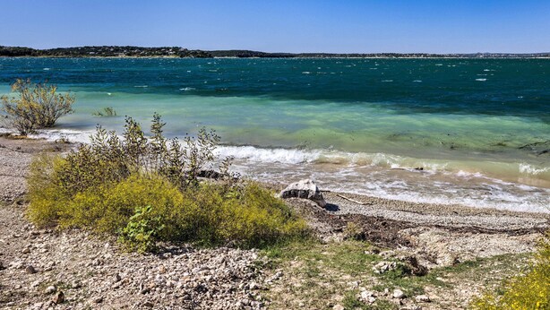 Un paysage côtier caractérisé par une eau claire, une rive rocheuse et une végétation clairsemée.