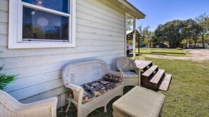 Une maison dotée d’un porche aménagé avec des meubles en osier, notamment un banc et une table.