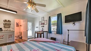 Une chambre à coucher avec un lit, un ventilateur de plafond, une télévision et une fenêtre avec des rideaux.