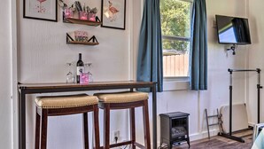 Une pièce avec une table en bois, deux tabourets de bar, un petit radiateur, un téléviseur fixé au mur et une fenêtre avec des rideaux.