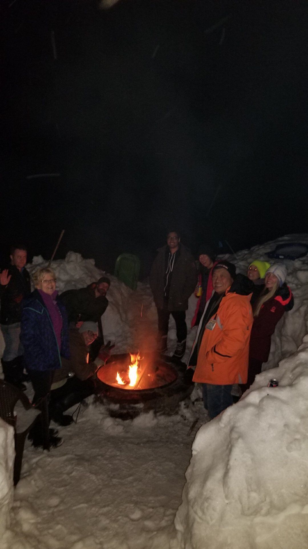 A group of people gathered around a campfire in a snowy outdoor setting.
