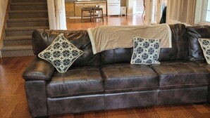 A living room with a leather sofa, a remote control on a coffee table, a staircase, a kitchen area, and a dining table. - SLOPES AND STREAMS (Searchmont)