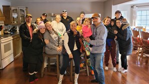 A group of people in a kitchen with wooden cabinets, a refrigerator, and a dining area with chairs. - SLOPES AND STREAMS (Searchmont)