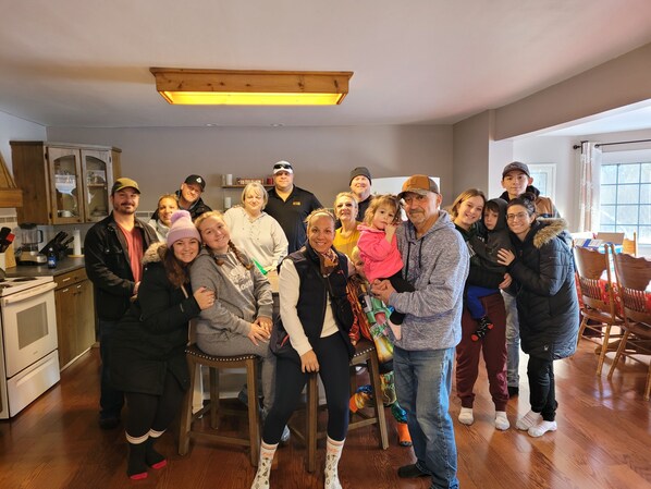 Un groupe de personnes se trouve dans une cuisine équipée de meubles en bois, d’un réfrigérateur et d’un coin repas avec des chaises.