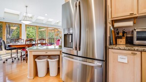 A modern kitchen with a stainless steel refrigerator, wooden cabinets, and a dining area with natural light. - Idyllic NatureEstate, Pool, Jacuzi, PuttGreen, Gardens (Lagunitas-Forest Knolls)
