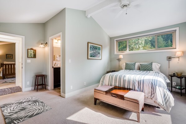 A bedroom with a bed, bedside tables, a nightstand, a window, and a door leading to another room.