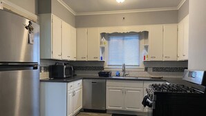 Een moderne keuken met witte kasten, roestvrijstalen apparatuur en een raam met jaloezieën.