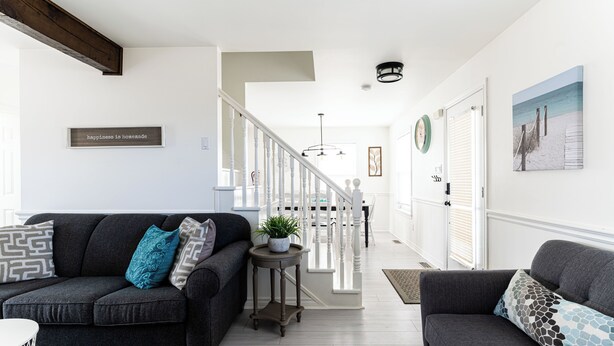 A modern living room with two dark grey sofas, a small round table with a plant, and a staircase leading to another level.