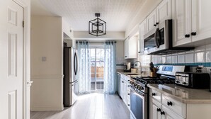 A modern kitchen with white cabinetry, a stainless steel refrigerator, a microwave, a stove, and a toaster.