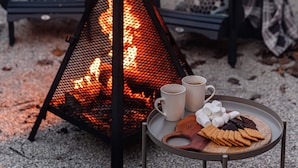 A cozy outdoor seating area with a fire pit, a table with snacks and drinks, and a chair with a blanket.
