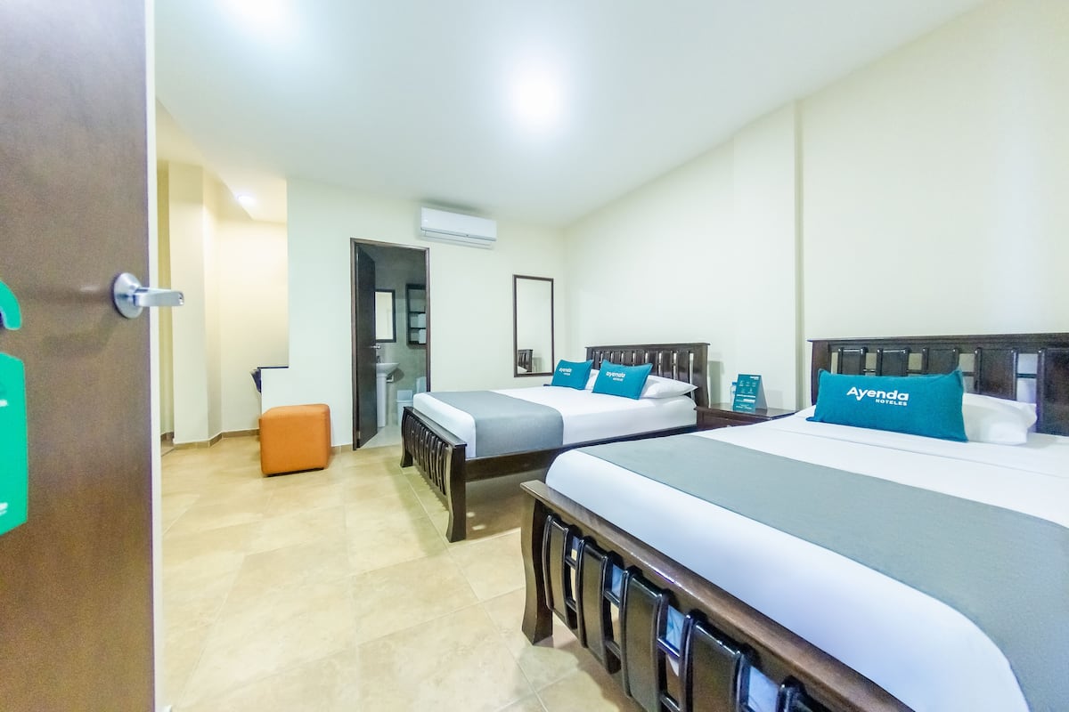 Une chambre d’hôtel avec deux lits, un petit pouf orange et une porte avec une enseigne verte.