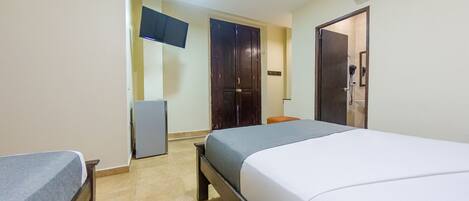 A hotel room with a bed, a desk, a chair, a wardrobe, and a TV on the wall.