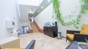 Ein geräumiger Innenbereich mit einer Treppe zu einer oberen Etage, einer Kaffeemaschine, einem Mülleimer und einem Korbsessel mit gelber Sitzkissen.