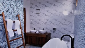 Un baño con tocador de madera, dos lavamanos, una bañera y un perchero para toallas.